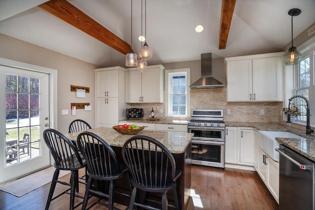 kitchen with lofted ceiling with beams, a sink, decorative backsplash, stainless steel appliances, and wall chimney range hood