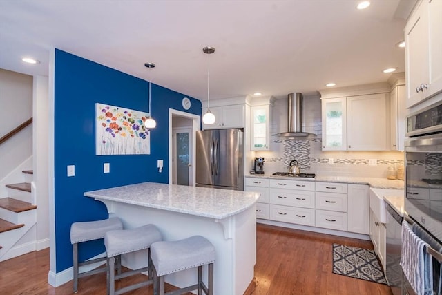 kitchen featuring pendant lighting, a breakfast bar area, white cabinetry, stainless steel appliances, and wall chimney exhaust hood