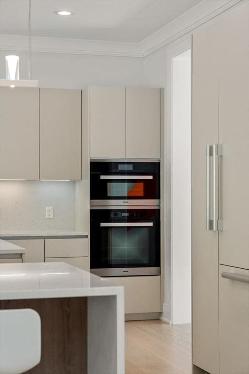 kitchen with crown molding, light countertops, double oven, light wood-style floors, and paneled refrigerator