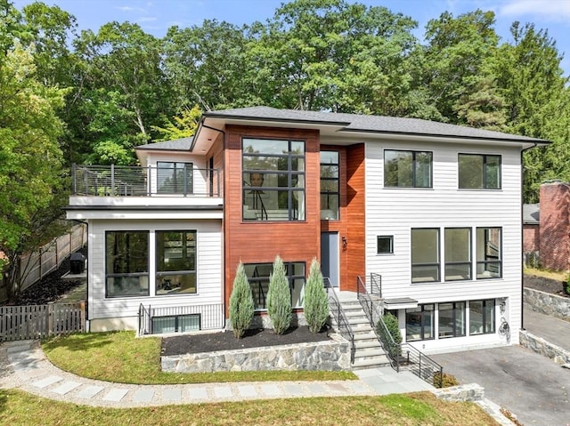 contemporary house featuring fence, a balcony, and stairs