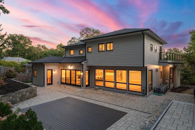 back of house at dusk featuring a patio area, fence, and a balcony