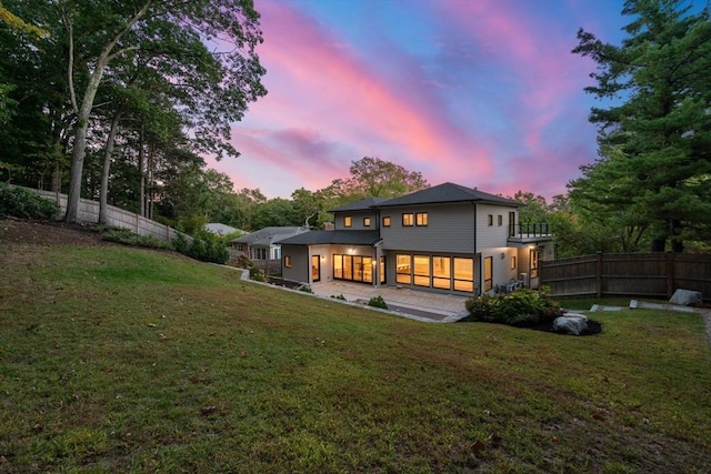 back of house at dusk featuring a patio area, fence, and a yard