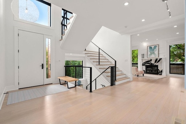 foyer entrance featuring recessed lighting, wood finished floors, stairs, a high ceiling, and a high end fireplace