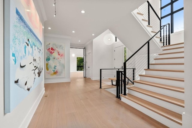 foyer entrance featuring crown molding, a healthy amount of sunlight, wood finished floors, baseboards, and stairs