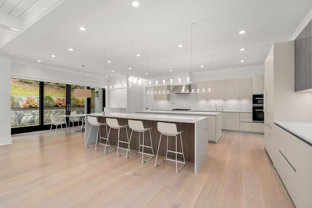 kitchen with a large island, light wood-style flooring, backsplash, modern cabinets, and wall chimney exhaust hood