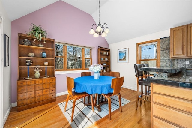 dining room with an inviting chandelier, baseboards, light wood-style floors, and vaulted ceiling