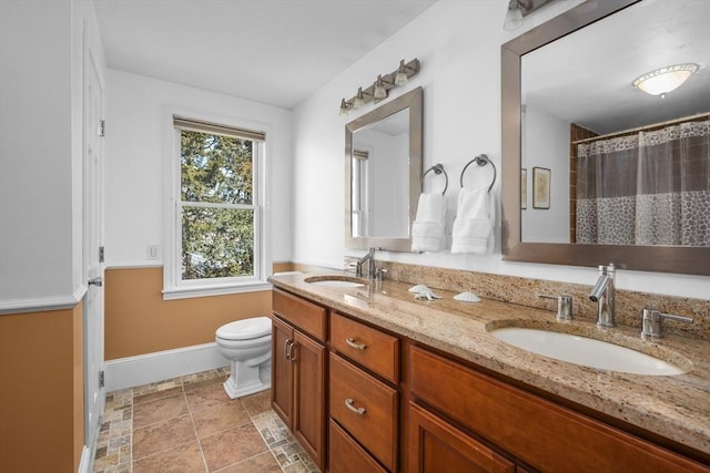 bathroom featuring double vanity, toilet, baseboards, and a sink