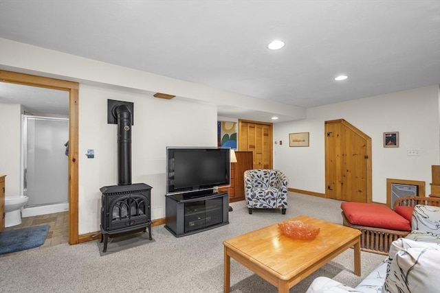 living room featuring recessed lighting, baseboards, light carpet, and a wood stove