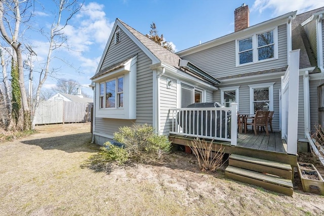 rear view of property featuring a wooden deck, roof with shingles, a chimney, and fence