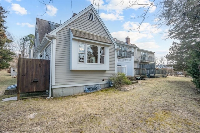 rear view of house featuring a lawn, a balcony, and roof with shingles