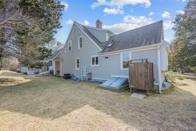 back of house featuring a chimney, a yard, and a shingled roof