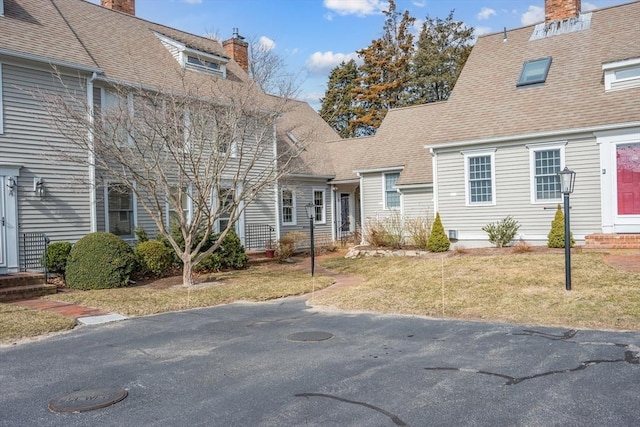 view of front of property featuring a chimney, entry steps, a shingled roof, and a front yard