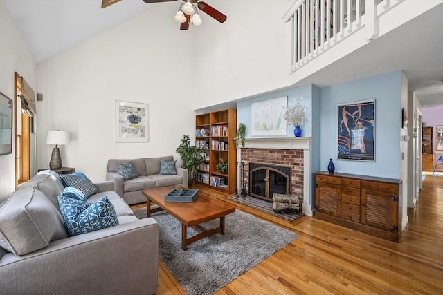 living room with a ceiling fan, a brick fireplace, wood finished floors, and high vaulted ceiling