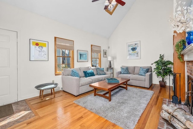 living area featuring ceiling fan, high vaulted ceiling, a brick fireplace, and wood finished floors