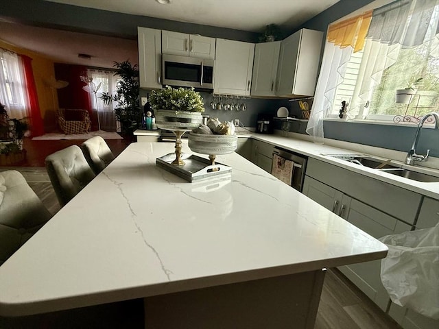 kitchen featuring a healthy amount of sunlight, a kitchen island, light stone countertops, a sink, and stainless steel appliances