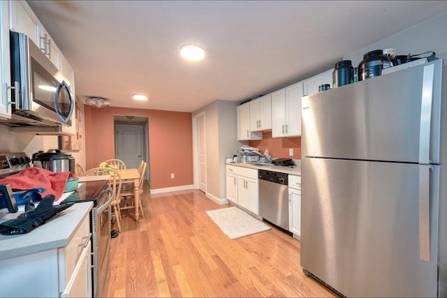 kitchen with stainless steel appliances, white cabinetry, and light hardwood / wood-style flooring