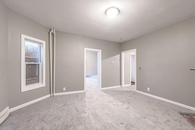 empty room with a baseboard heating unit, baseboards, and carpet