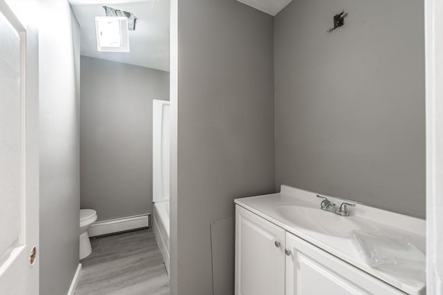 bathroom with toilet, wood finished floors, baseboard heating, a tub, and vanity