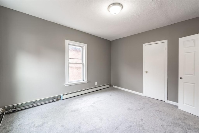 carpeted spare room with a textured ceiling, baseboards, and a baseboard heating unit