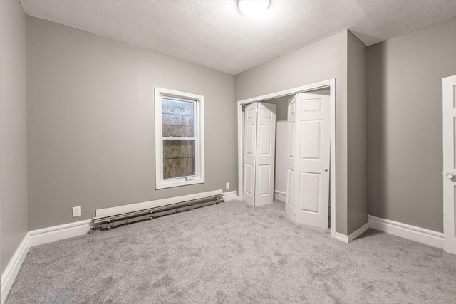 unfurnished bedroom featuring baseboard heating, a closet, a textured ceiling, baseboards, and carpet flooring