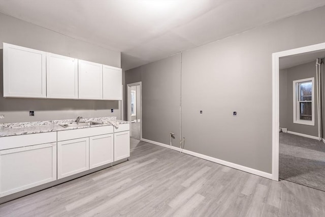 kitchen featuring a sink, baseboards, light wood-type flooring, and white cabinets