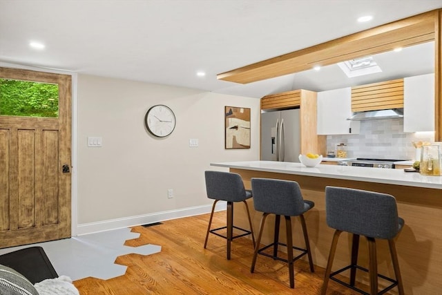 616 Grove St, Framingham, MA 01701 - kitchen featuring stainless steel refrigerator with ice dispenser, a breakfast bar, light countertops, decorative backsplash, and light wood-style flooring
