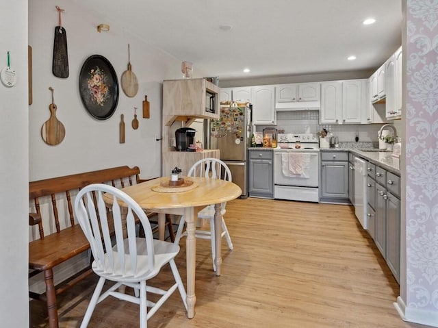 kitchen featuring white appliances, gray cabinetry, light wood-type flooring, a sink, and light stone countertops