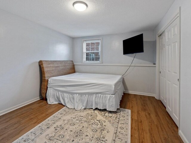 bedroom featuring wood finished floors, a textured ceiling, a closet, and baseboards