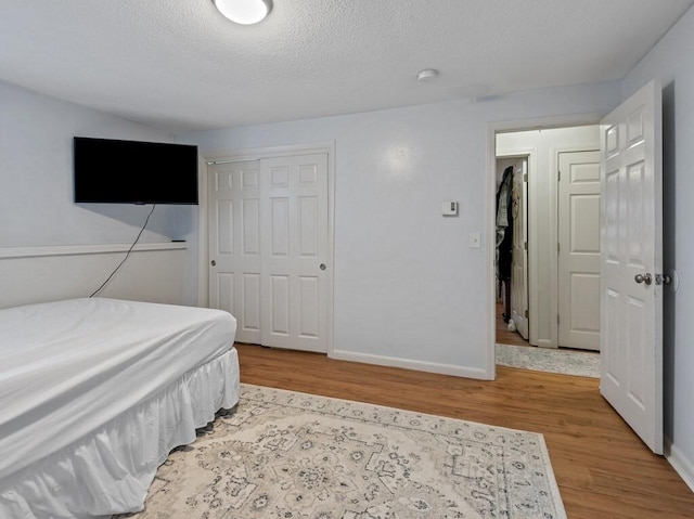 bedroom with wood finished floors, a closet, baseboards, and a textured ceiling