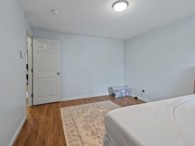 bedroom with wood finished floors, a textured ceiling, and baseboards