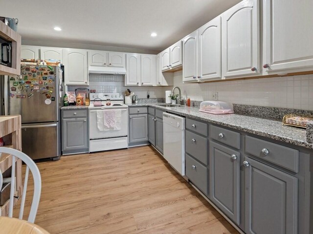 kitchen featuring gray cabinetry, white appliances, a sink, under cabinet range hood, and light wood finished floors