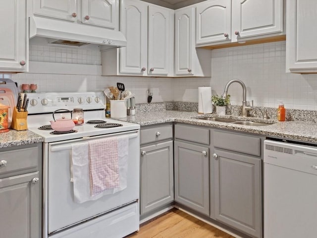 kitchen with white appliances, under cabinet range hood, gray cabinets, a sink, and decorative backsplash