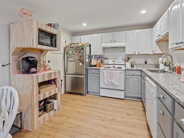 kitchen featuring white appliances, gray cabinetry, a sink, under cabinet range hood, and light wood finished floors