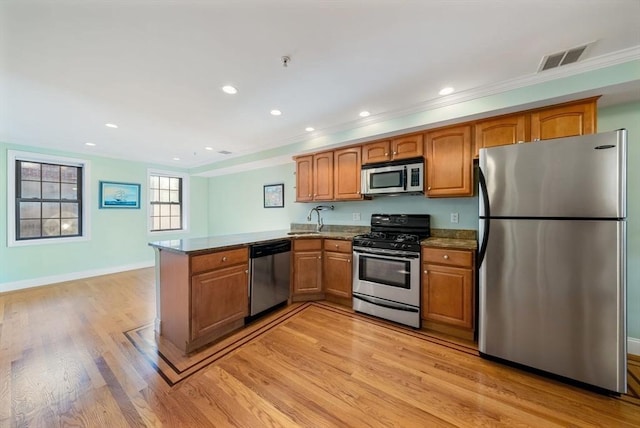 kitchen with stainless steel appliances, a peninsula, a sink, visible vents, and brown cabinetry