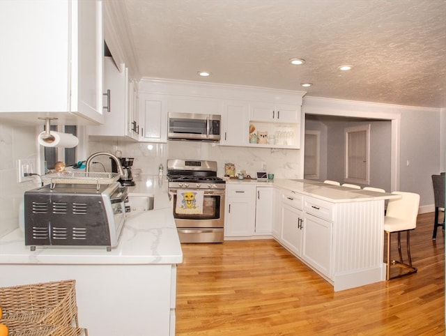 kitchen with kitchen peninsula, white cabinets, stainless steel appliances, and light wood-type flooring