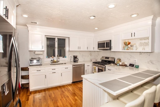 kitchen with kitchen peninsula, appliances with stainless steel finishes, sink, light hardwood / wood-style flooring, and white cabinets