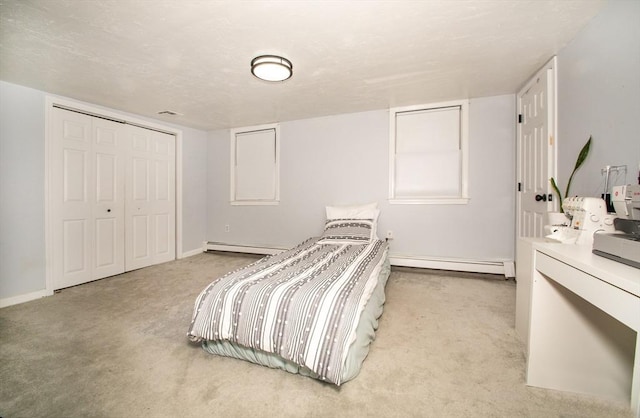 bedroom with a closet, light colored carpet, and a baseboard heating unit