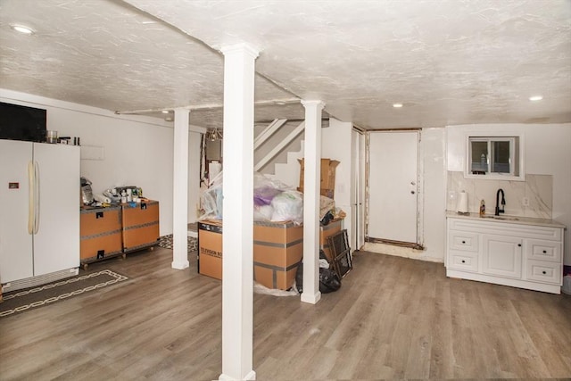 basement with sink, light hardwood / wood-style floors, a textured ceiling, and white refrigerator