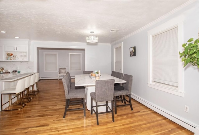 dining room featuring a textured ceiling, light wood-type flooring, a baseboard radiator, and ornamental molding