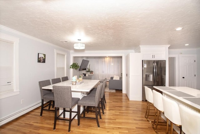 dining space featuring ornamental molding, a textured ceiling, light hardwood / wood-style flooring, and a baseboard heating unit