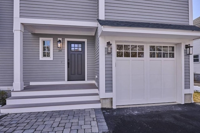 doorway to property with driveway, a shingled roof, and an attached garage