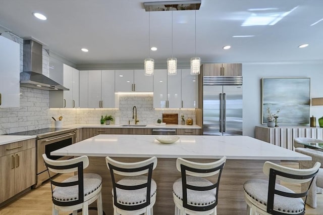 kitchen featuring stainless steel appliances, a sink, a kitchen breakfast bar, wall chimney exhaust hood, and modern cabinets