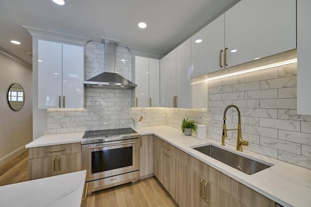 kitchen featuring wall chimney range hood, modern cabinets, stainless steel electric range, and a sink