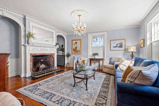 living room with an inviting chandelier, arched walkways, a fireplace with flush hearth, and wood finished floors