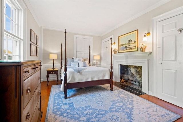 bedroom with baseboards, ornamental molding, wood finished floors, and a fireplace