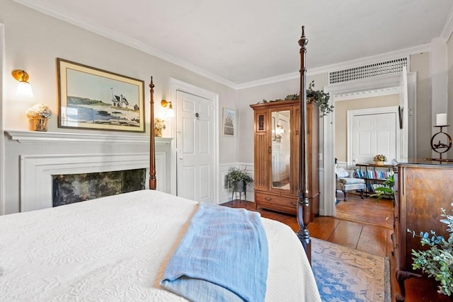 bedroom featuring visible vents, crown molding, a tiled fireplace, wainscoting, and wood-type flooring