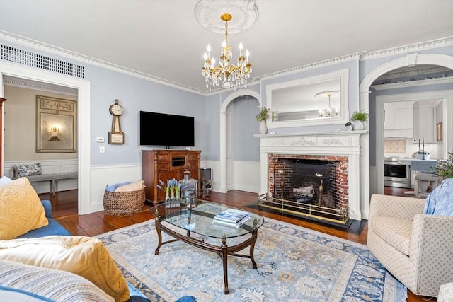 living room with wainscoting, arched walkways, a fireplace with flush hearth, wood finished floors, and visible vents