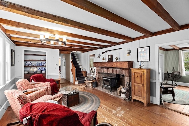 living room with stairway, a wood stove, hardwood / wood-style floors, an inviting chandelier, and beam ceiling