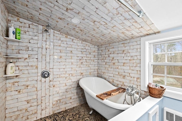 full bathroom with brick wall, a freestanding tub, tiled shower, and vaulted ceiling