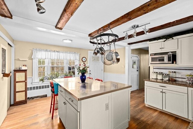 kitchen with radiator, stainless steel microwave, a kitchen island, beam ceiling, and light wood-style floors
